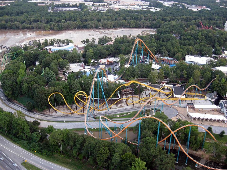 Aerial view of an amusement park and roller coasters situated alongside a swollen, flooded river
