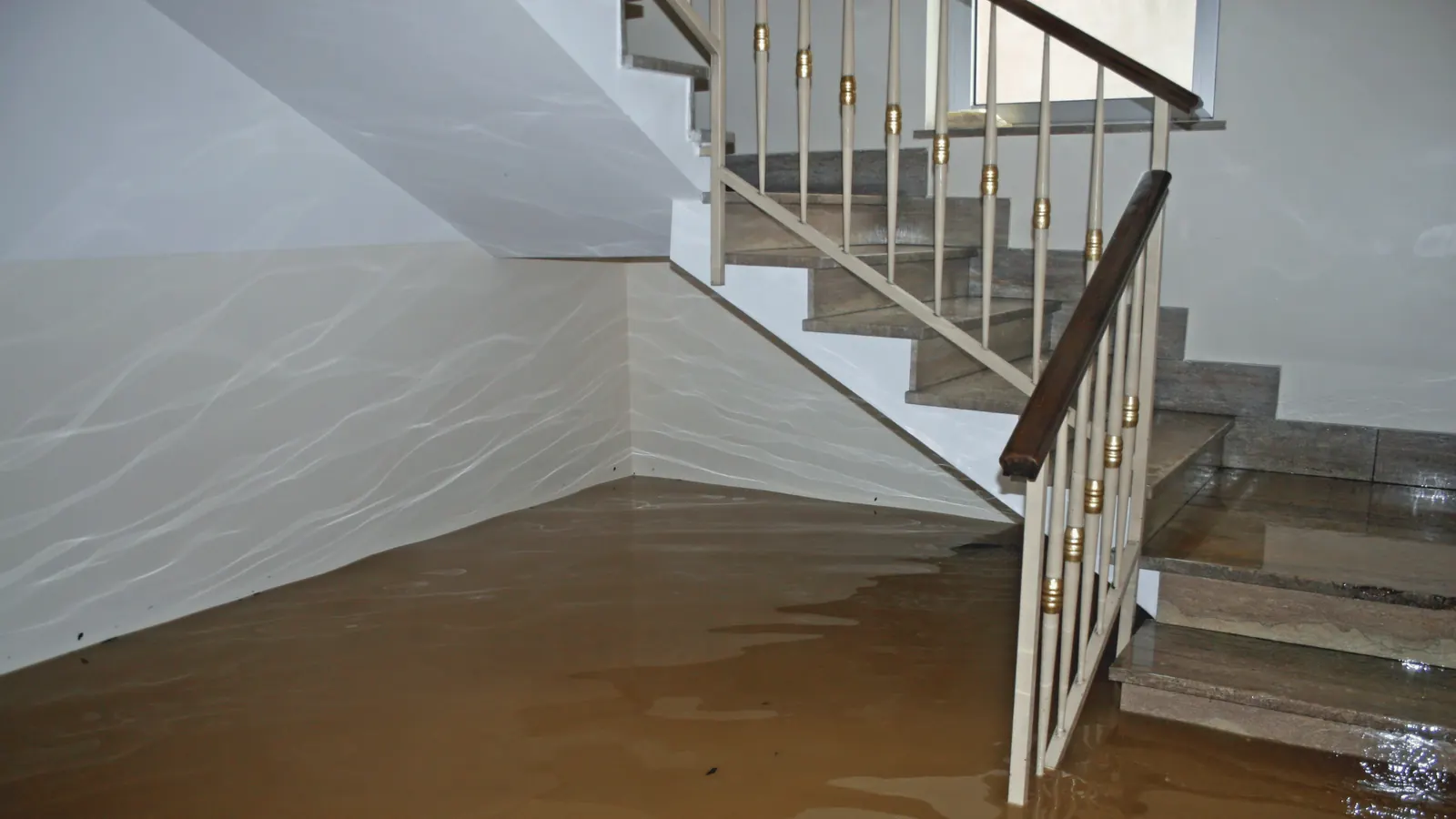 Flooded interior room with water pooling near wooden staircase