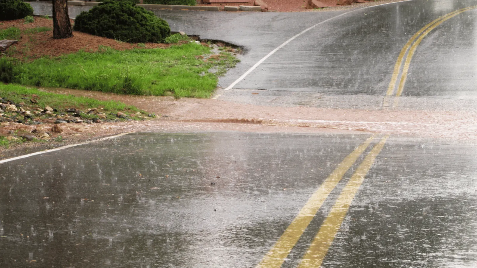 Heavy rainfall runoff flowing along asphalt road and curb