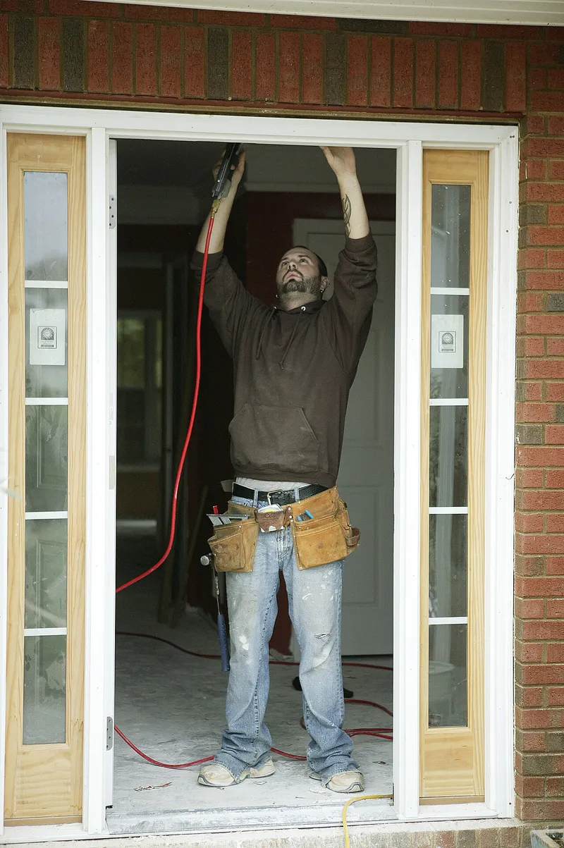 Worker in a tool belt installing door trim in a residential entryway (FEMA photo by Andrea Booher)